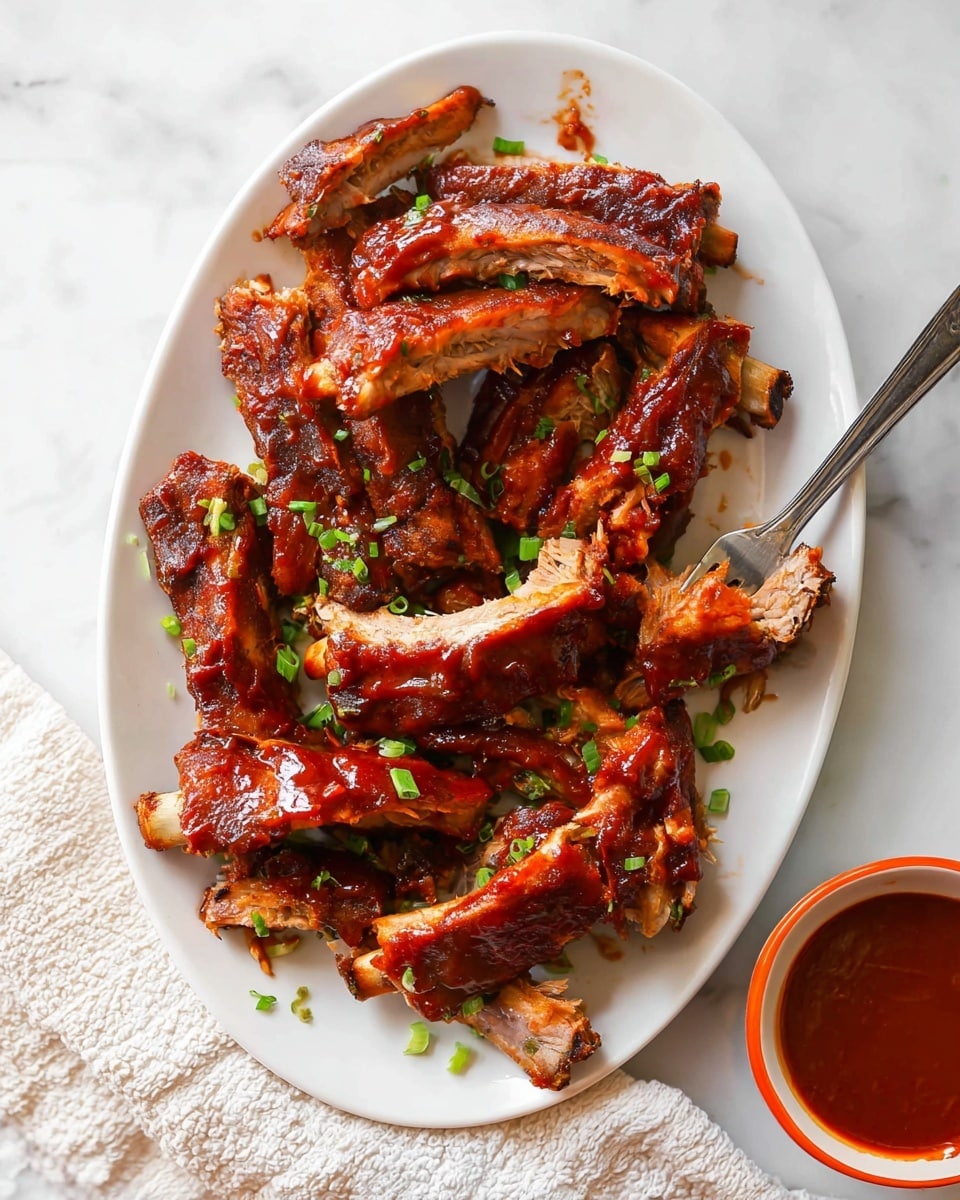A white oval plate holds around a dozen barbecue ribs stacked in a slightly messy pile, each rib covered in thick, glossy dark red barbecue sauce that glistens under the light. Small pieces of chopped green onion sprinkle over the ribs, adding a fresh green contrast to the rich red glaze. A small metal fork with a black handle rests on the right side of the plate, piercing one rib. Below the plate is a small white bowl with a bright orange rim, filled with more barbecue sauce. The whole scene is set on a white marbled surface with a textured white cloth partially visible in the lower right corner. photo taken with an iphone --ar 4:5 --v 7