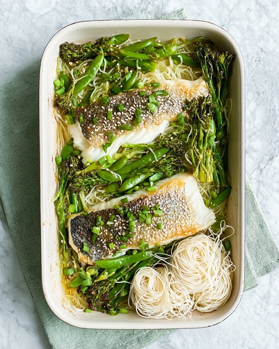 The image shows a white rectangular baking dish filled with two cooked fish fillets placed on top of green vegetables including snap peas, broccolini, and asparagus, all with a slight grill or roast texture. On the right side of the dish, there are three small bundles of thin white noodles with a soft, delicate texture. The fish fillets have a golden-brown crispy skin with some sesame seeds sprinkled on top, along with scattered chopped green onions. The dish is set on a light green cloth over a white marbled surface. Photo taken with an iphone --ar 4:5 --v 7
