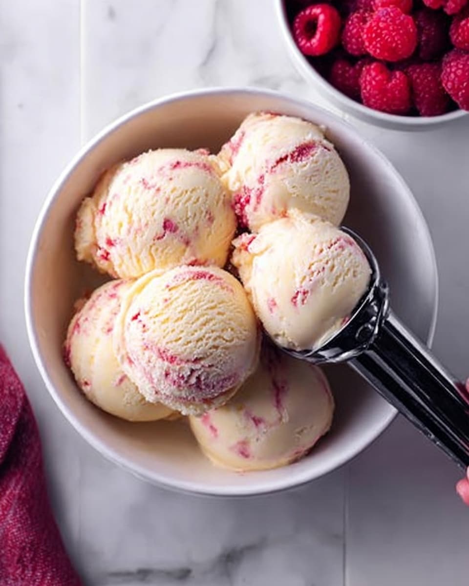 A white bowl filled with five smooth and creamy scoops of pale yellow ice cream with pinkish-red swirls on a white marbled surface, with a black ice cream scooper held by a woman's hand lifting one scoop from the bowl; a white bowl of fresh red raspberries is partially visible on the top right corner. photo taken with an iphone --ar 4:5 --v 7