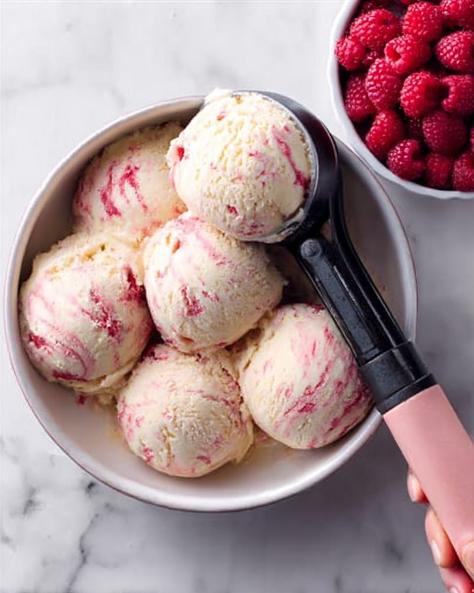 The image shows five scoops of creamy ice cream with swirls of pink and white, placed inside a round white bowl. A scoop is being lifted by a woman's hand holding a black ice cream scooper with a pale pink handle. To the right of the bowl, there is a white bowl filled with fresh red raspberries. The background is a white marbled surface. photo taken with an iphone --ar 4:5 --v 7