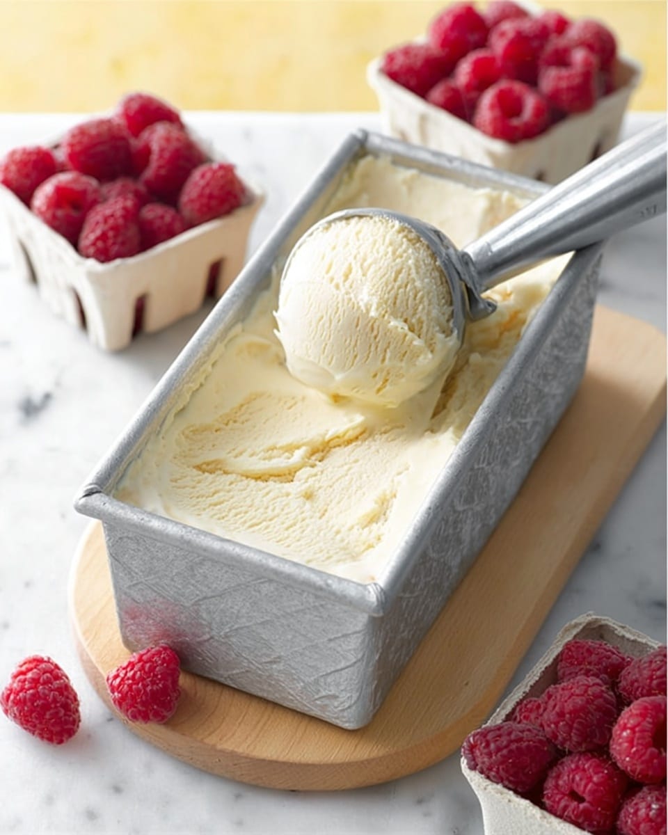 A rectangular metal container filled with creamy pale yellow ice cream, one scoop lifted by a metal ice cream scoop resting on top, placed on a light wooden board. Around the container are three white cardboard containers filled with bright red raspberries, with a few loose raspberries scattered on the wooden board. The background and surface are a white marbled texture with a soft yellow tone behind. Photo taken with an iphone --ar 4:5 --v 7