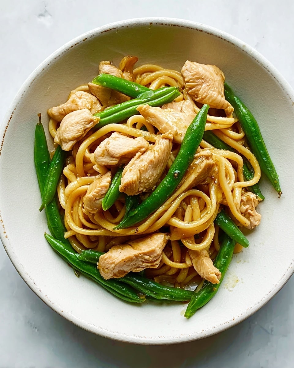 A white bowl on a white marbled surface holds a simple dish of noodles, chicken, and green beans. The bottom layer consists of thick, light brown noodles twisted and coiled, creating a soft base. Scattered on top are medium-sized, cooked chicken pieces with a light golden-brown color and a slightly shiny texture. Bright green beans are placed evenly around and on top of the chicken, adding a fresh contrast. The overall look is neat and light without any sauce visible. photo taken with an iphone --ar 4:5 --v 7