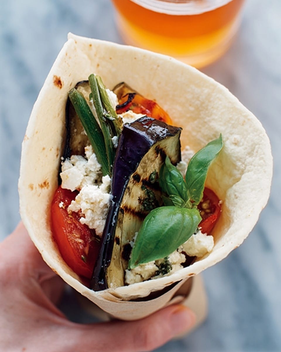 A soft white tortilla is folded in a cone shape, holding several layers inside. The bottom layer is a grilled red tomato, above it is crumbled white cheese scattered unevenly. On top, there are grilled green onions and slices of grilled purple eggplant with dark grill marks. A few fresh green basil leaves rest on the side and inside the cone. The tortilla wrap is held by a woman's hand, set against a smooth white marbled surface. A glass with orange liquid sits near the wrap. Photo taken with an iphone --ar 4:5 --v 7