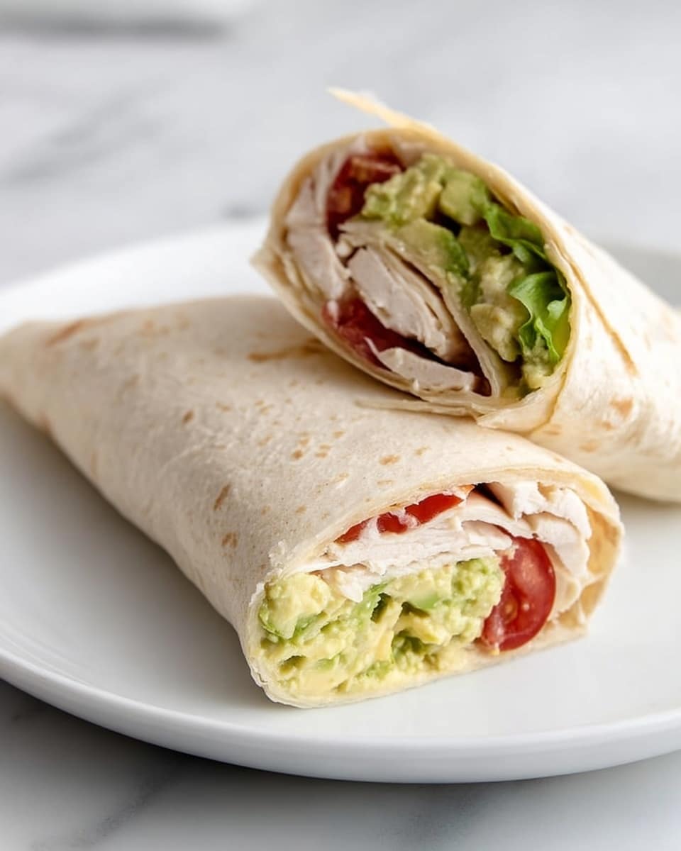 The image shows a close-up of two tortilla wraps placed on a white plate with a white marbled surface underneath. One wrap is whole and folded, with a pale beige, soft tortilla covering the ingredients inside. The other wrap is sliced in half, showing three distinct layers inside: a bottom layer of green mashed avocado with a creamy texture, a middle layer of white turkey or chicken slices, and a top layer with bright red tomato pieces. The colors and textures contrast nicely within the clear sections of the wrap, making it look fresh and tasty. Photo taken with an iphone --ar 4:5 --v 7