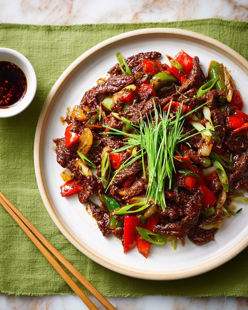 A white plate sits on a green cloth over a white marbled table, holding a stir-fried dish with three main layers: the bottom layer is dark brown crispy strips of meat coated in a shiny sauce, mixed with chunks of bright red bell pepper and light green scallion pieces scattered throughout. On top, there is a small pile of fresh, long green chives placed in the center. To the right of the plate are light wooden chopsticks resting on the table, and above the green cloth is a small white bowl filled with dark sauce, edged with red seasoning. Photo taken with an iphone --ar 4:5 --v 7