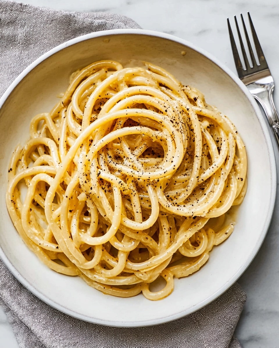A white bowl filled with thick, twisted spaghetti coated in a light sauce, showing a glossy texture. The pasta is arranged in loose loops and topped with freshly ground black pepper, scattered unevenly across the surface, adding specks of dark color. The bowl sits on a white marbled surface next to a silver fork on a pale textured cloth. The overall look is simple, clean, and appetizing, with a focus on the noodles and pepper as the main visual elements. photo taken with an iphone --ar 4:5 --v 7