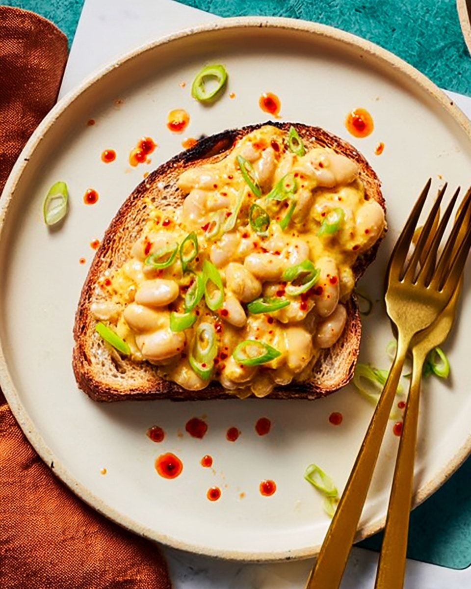 A slice of toasted brown bread is placed in the center of a white plate, topped with a thick, creamy macaroni and cheese mixture. The macaroni is coated in a pale yellow cheese sauce, sprinkled with chopped green onions, and drizzled with small drops of red hot sauce around and on top of the mac and cheese. A golden fork and knife are laid side by side on the right edge of the plate. The plate sits on a bright blue surface, adding a strong contrast to the food. Photo taken with an iphone --ar 4:5 --v 7