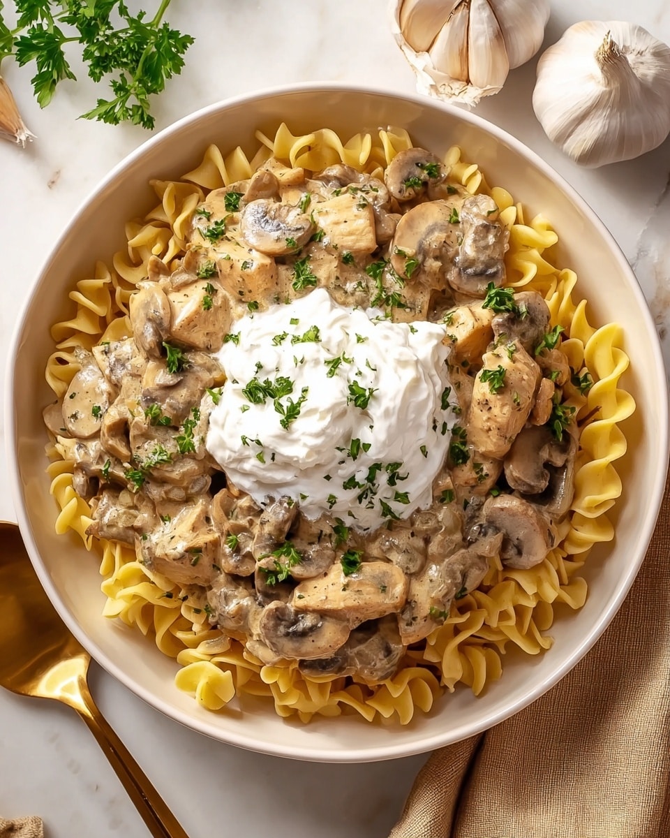 A white bowl is filled with three layers of food: the bottom layer is yellow curly egg noodles with a smooth texture, the middle layer contains creamy mushroom and chicken pieces mixed together in a light brown sauce, and the top layer has a swirl of white sour cream placed in the center, sprinkled with chopped green parsley all over. The bowl is set on a white marbled surface, accompanied by a golden spoon on the side and a garlic bulb in the corner, giving a fresh and warm feeling. photo taken with an iphone --ar 4:5 --v 7