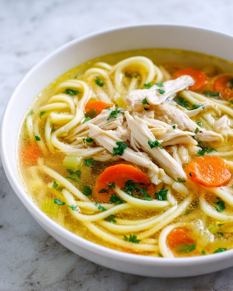 A white bowl filled with clear golden broth, layered with creamy white spiral noodles along the bottom, large bright orange carrot slices placed on top, light green celery pieces scattered around, and shredded pale chicken meat arranged in the center. Small dark green parsley leaves are sprinkled throughout the soup, adding texture and color contrast. The bowl sits on a white marbled surface. photo taken with an iphone --ar 4:5 --v 7