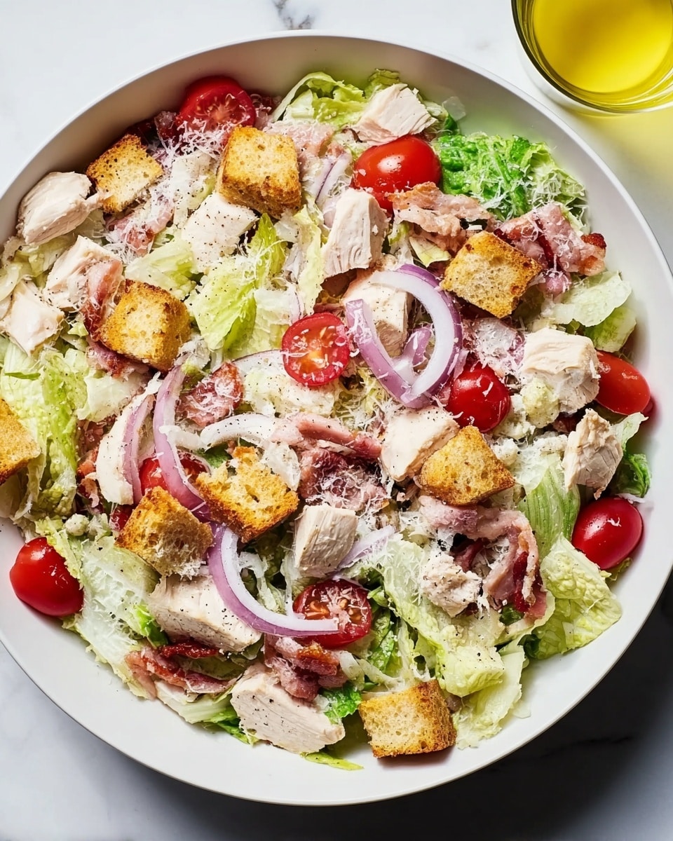 A white bowl filled with a fresh salad showing several layers: at the bottom, bright green romaine lettuce leaves create a leafy base; chunks of pale pink cooked chicken are scattered evenly on top; around them are halved bright red cherry tomatoes and thin slices of light purple onion rings; small golden brown croutons are spread across the salad; tiny pieces of crispy reddish bacon add texture; finally, a light sprinkle of shredded white cheese is on the very top. The bowl is placed on a surface with a white marbled texture. photo taken with an iphone --ar 4:5 --v 7
