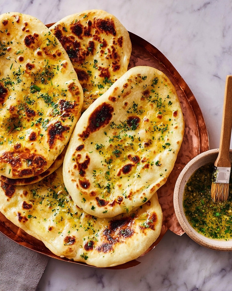 The image shows several pieces of flatbread, all placed overlapping on a white marbled surface with a copper tray beneath some of them. Each flatbread has a golden-brown color with darker charred spots and is sprinkled with finely chopped green herbs. To the side, there is a white bowl filled with greenish garlic butter sauce and a wooden brush resting inside it. The textures of the flatbreads are slightly puffy with some bubbles and uneven surfaces. photo taken with an iphone --ar 4:5 --v 7