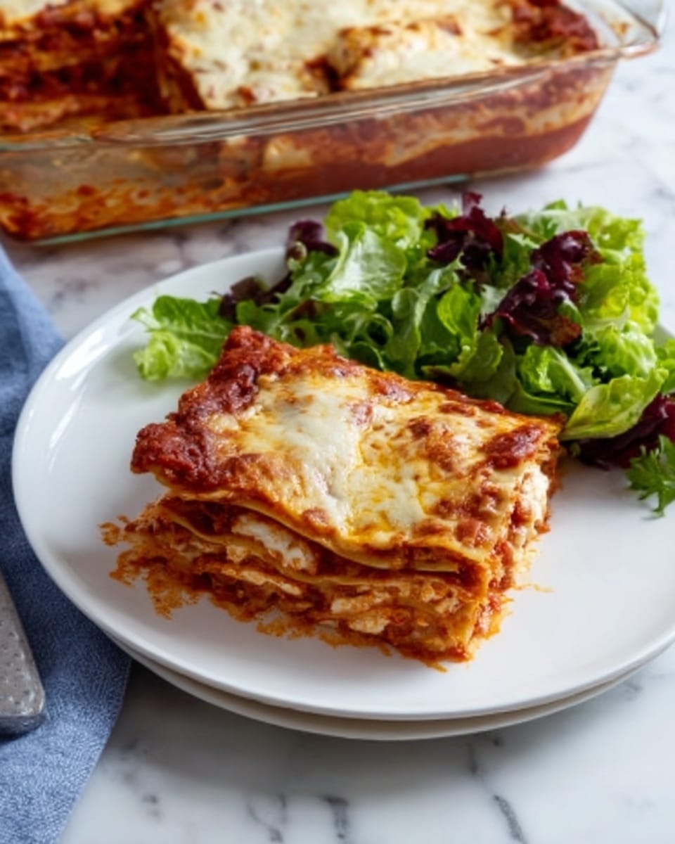 A slice of lasagna with four visible layers sits on a white plate, each layer showing a rich red tomato sauce with browned melted cheese on top. The pasta layers are thin and slightly golden, with the cheese layer on top bubbly and slightly browned. To the side of the lasagna is a fresh green salad with leafy lettuce. In the background, a glass baking dish filled with more lasagna can be seen resting on a blue cloth, all on a white marbled surface. photo taken with an iphone --ar 4:5 --v 7